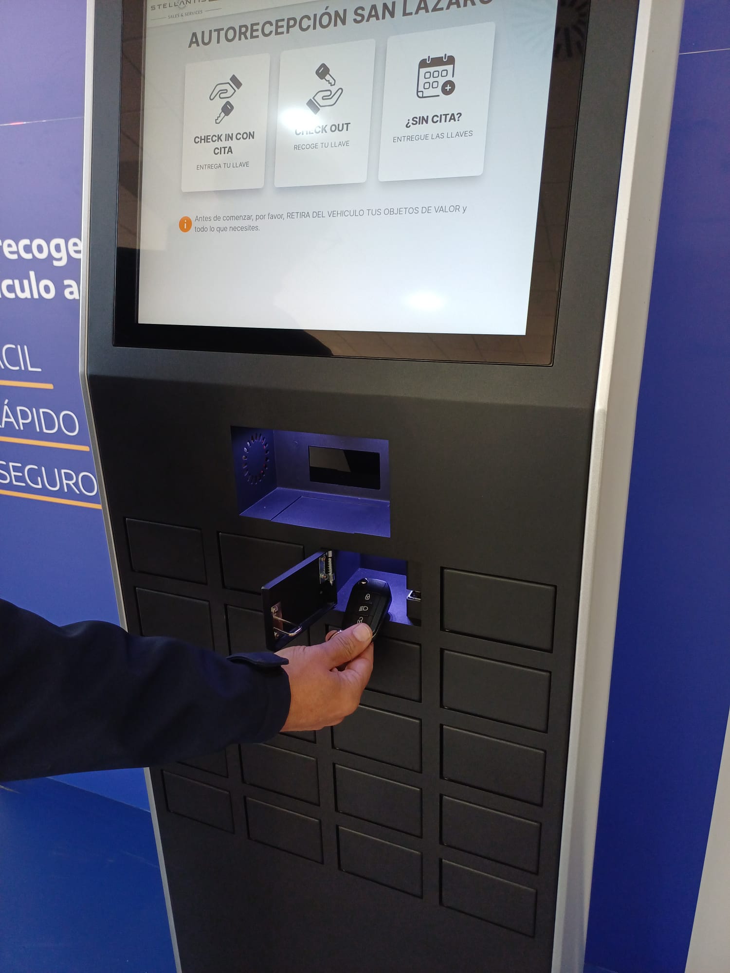 Personuses a self-service kiosk to check in/out, inserting a key into the reader beneath a touchscreen displaying options in Spanish.